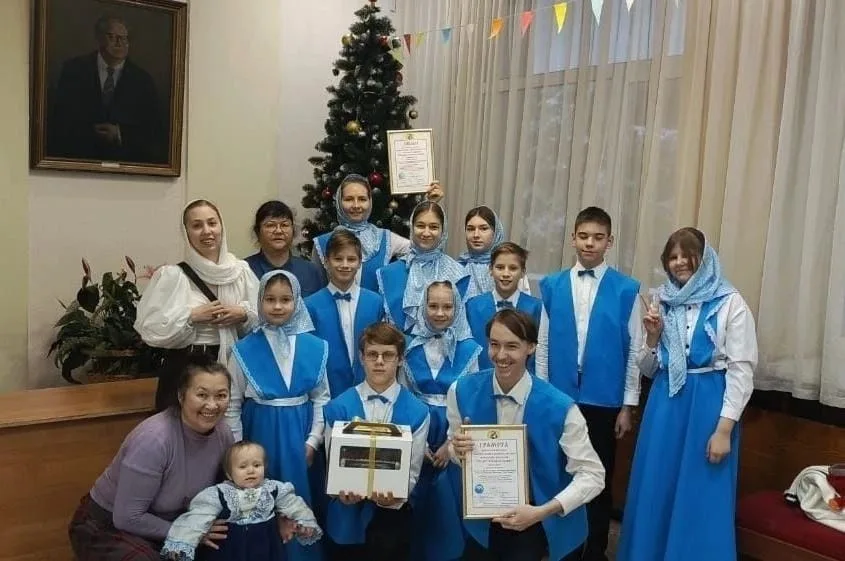 Группа детей в синих концертных костюмах хора стоит с грамотами и руководителем